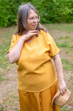 Şık, yaşlı, mutlu, sarı kıyafetli, şapkalı, hardallı, açık havada gülümseyen olgun bir kadın. Yaz ya da bahar, doğal görünüş, günlük yaşam tarzı, gerçek kadınlar için moda.