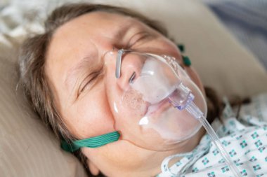 Yatakta oksijen maskeli kadın hasta, insan merkezli sağlık desteği, solunum desteği, klinik havalandırma arayüzü tıkanık uyku apnesi tedavisi, hastanede tıbbi solunum cihazları.