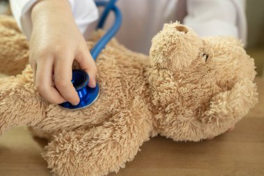 Küçük çocuk, sarışın kız 4 yaşında oyuncakla oynuyor, küçük doktor oyuncak ayıyı tedavi ediyor, mutlu çocukluk, mesleki rehberlik, peluş arkadaş