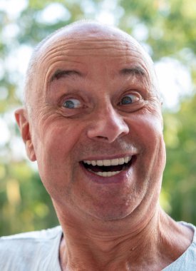 Yaşlı beyaz adam komik yüz ifadesi yapıyor, detaylı görünüm burun dudak ağız, deri dokusu sakalı, komik yüz ifadesi duyguyu, abartılı yüz hatlarını, vücut dilini gösteriyor.