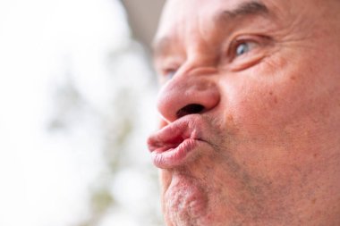 Yaşlı beyaz adam komik yüz ifadesi yapıyor, detaylı görünüm burun dudak ağız, deri dokusu sakalı, komik yüz ifadesi duyguyu, abartılı yüz hatlarını, vücut dilini gösteriyor.