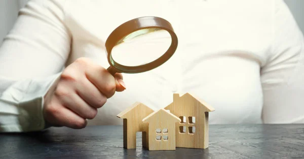 A woman is holding a magnifying glass over a wooden houses. Real estate appraiser. Property valuation / appraisal. Find a house. Search for housing. Real estate market analysis. Selective focus