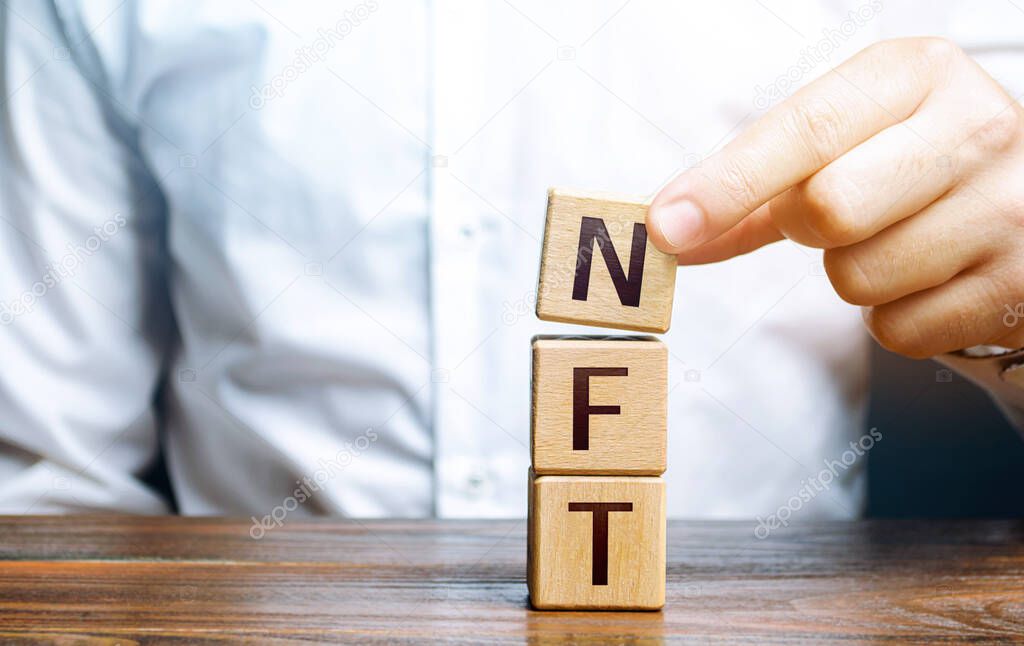 Man puts together word NFT from blocks. NFT non-fungible token. Selling digital art assets through internet auctions. Blockchain technology. Monetization, investment in cryptographic tokens