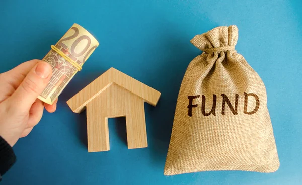 Money bag with the word Fund, wooden house and euro bills in hand. Real estate investment concept. Projects, construction and operation of real estate objects. Business and finance. Housing market