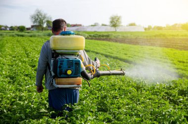 A farmer with a mist fogger sprayer sprays fungicide and pesticide on potato bushes. Effective crop protection, environmental impact. Protection of cultivated plants from insects and fungal infections clipart