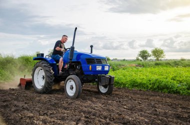 Farmer on tractor cultivates farm field. Milling soil, crushing and loosening ground before cutting rows. Farming, agriculture. Preparatory earthworks before planting a new crop. Land cultivation clipart