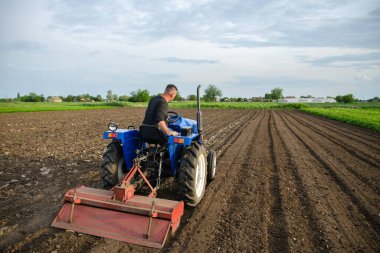 A farmer cultivates a field with a tractor after harvest. Milling soil, crushing before cutting rows. Farming, agriculture. Loosening surface, land cultivation. Plowing field. Removing roots clipart