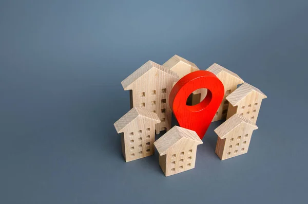 Wooden houses and a red location pin. Location, accessibility to infrastructure. Residential complex. City navigation, orienteering. Search for housing options. Moving to a different city.