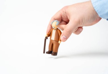 Bir el, bastonlu yaşlı bir adamın heykelini yerleştirir. Emekliler ve yaşlılar. Büyükbaba figürü. Bakım planlaması yaşlılara saygı ve desteği yansıtır.