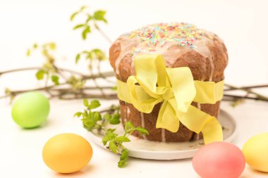 Paskalya pastası sarı kurdele ile süslenmiştir. Masanın üzerinde boyanmış yumurtalar var.