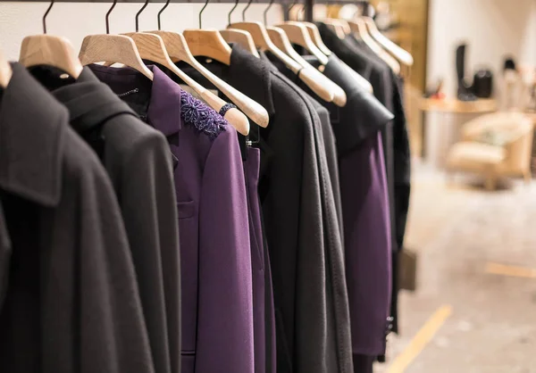 Ropa clásica para mujer en una percha en una boutique. Tonos púrpura y negro de la colección. Chaquetas, abrigos, vestidos — Foto de Stock