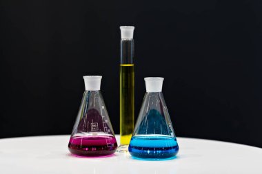 Kimya laboratuarı için ekipman. Mavi, kırmızı ve sarı reaksiyonlu cam mataralar masanın üzerinde duruyor..