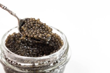Cam kavanoz premium siyah beluga havyarı ve içi yumurta dolu küçük gümüş bir kaşık. Beyaz arkaplan, yazı için yer