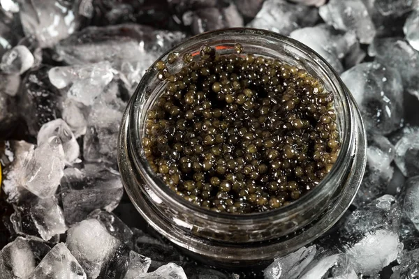 De zwarte kaviaar van de steurvis in een glazen pot wordt op het gemalen ijs gelegd. Bovenaanzicht, copyspace — Stockfoto