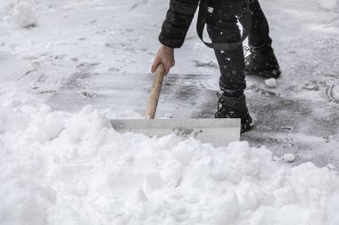 Bir adam kardan çıkan yolu büyük bir kürekle temizler. Kaldırımda derin sürüklenmeler.