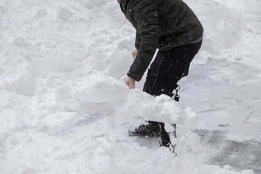 Bir adam kardan çıkan yolu büyük bir kürekle temizler. Kaldırımda derin sürüklenmeler.
