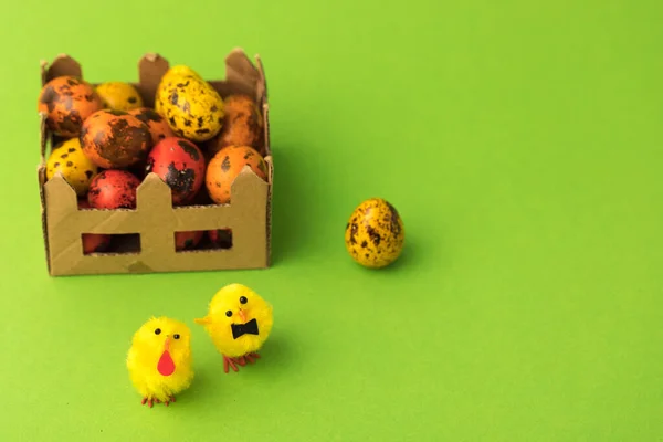 Little toy chickens on a green paper background as a Concept of Easter. Mesh and painted quail eggs.