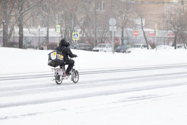 13.02.2021, Rusya, Moskova. Bisikletli bir yiyecek teslimatçısı kışın yolu geçer. Kar ve kar yağışı