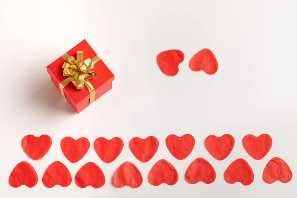Dos filas de corazones rojos de papel. Una caja con un arco de regalo y dos corazones al lado de un fondo blanco, —  Fotos de Stock