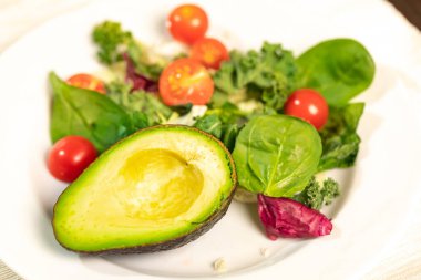 Taze yeşil marul yaprakları, kiraz domatesleri, salatalık ve avokado dilimleri bir tabakta.