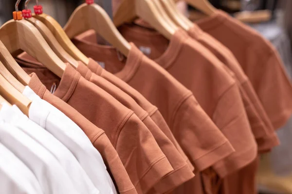 Tişörtler, mağazada askıda asılı erkekler ve kadınlar için yazlık giysiler. Beyaz ve bej. — Stok fotoğraf