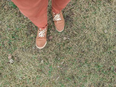 Spor ayakkabıları ayakları üzerinde kahverengi renktedir. Kahverengi pantolonlu insan yeni bahar çimlerinde duruyor.