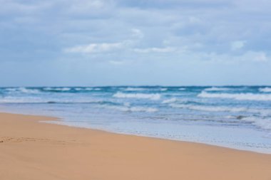 Gökyüzü ve ufukta bulutlar olan tropik okyanus plajı. Dalgaların kıyıya vurması, sudaki ince sarı kum.