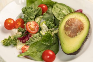 Masanın üzerinde yeşil salata yaprakları, yarım avokado, vişneli domatesler....
