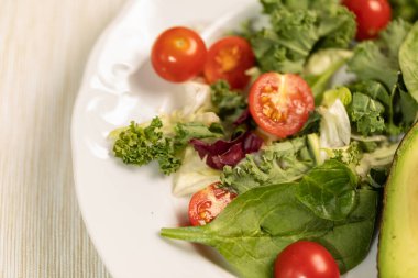 Taze yaprak salatası, kiraz domatesleri, salatalık ve avokado ile beyaz tabak. Uygun dengeli detoks diyeti.
