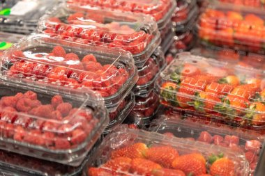 Vitrindeki plastik pakette taze, sulu çilek ve ahududu.