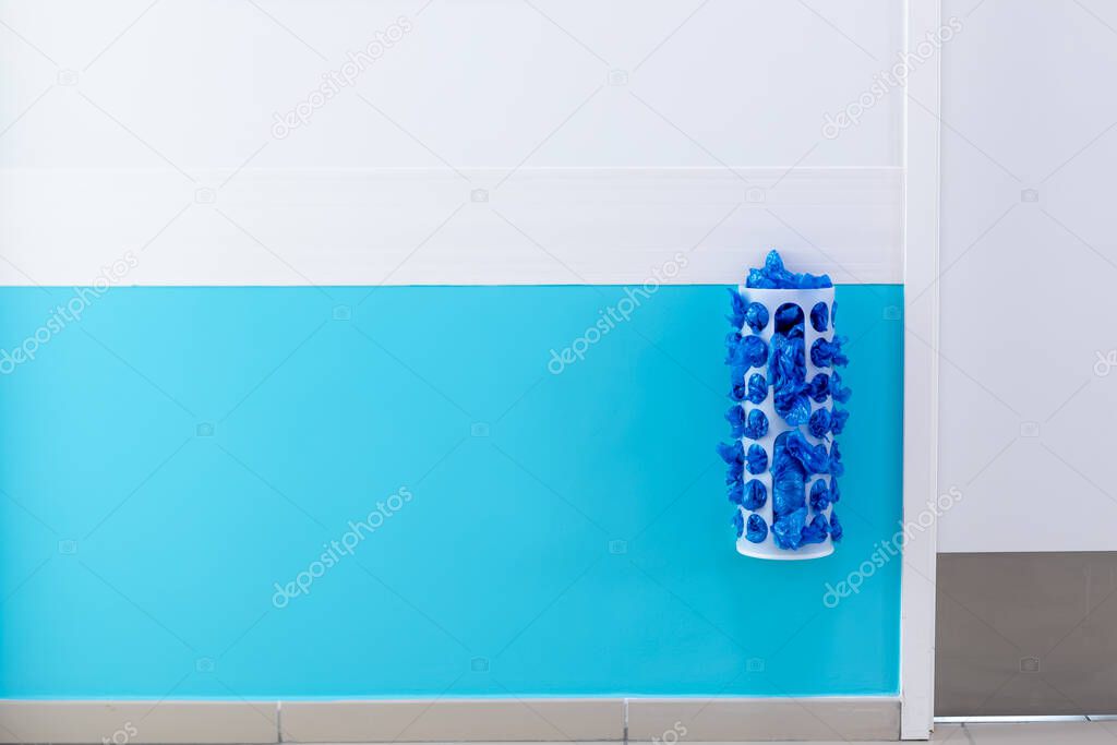 A dispenser with shoes on the wall at the medical facility. Blue and white wall paint,