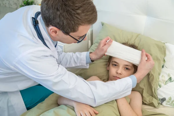 Ο παιδογιατρός βάζει έναν επίδεσμο ψύξης στο κεφάλι του παιδιού σε υψηλή θερμοκρασία. Τηλεφωνώ στο γιατρό στο σπίτι.. — Φωτογραφία Αρχείου