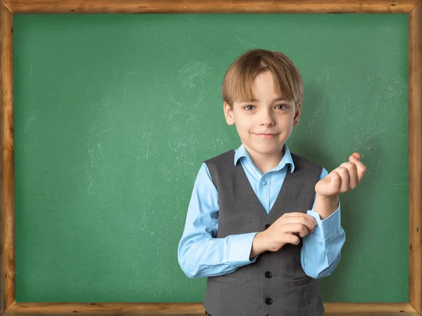 Concept Back to School. Garoto caucasiano em meio a uma placa de sala de aula em um uniforme escolar se prepara para responder — Fotografia de Stock