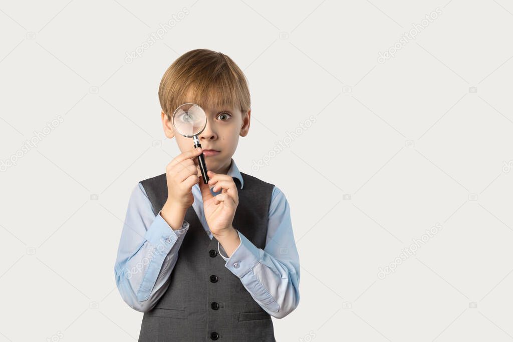 Caucasian boy in school uniform with a magnifying glass in front of his face.