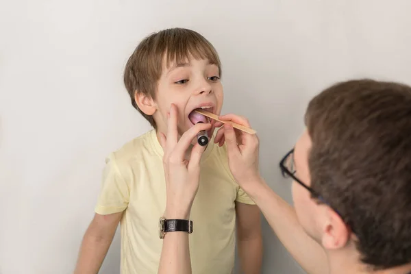 Vyšetření krku, úst a dítěte lékařem. Chlapec otevřel ústa dokořán, aby si prohlédl mandle.. — Stock fotografie