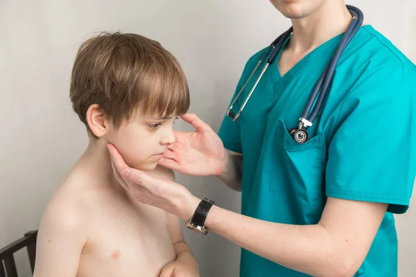 O pediatra examina os gânglios linfáticos e garganta do paciente meninos na clínica no escritório — Fotografia de Stock