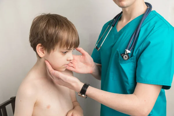 Çocuk doktoru ofisteki klinikteki erkek hastaların lenf nodlarını ve boğazlarını muayene ediyor.