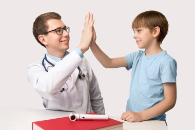 Beyaz arka planda beyaz bir erkek hasta ile beyaz doktor pratiği yapan çocuklar. Gülümseyen insanlar neşeyle beşlik çakar..