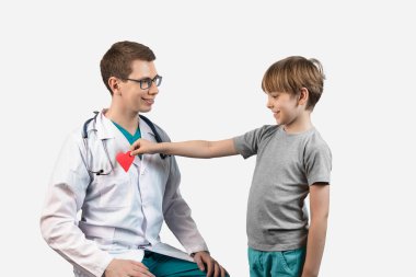 Beyaz arka planda bir erkek hasta olan bir çocuk doktoru portresi. Çocuk doktora oyuncak kırmızı bir kalp verir..