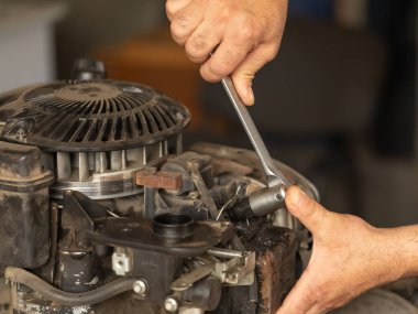 Bir adam benzin çim biçme makinesinin motorunu tamir ediyor. İngiliz anahtarını tutan eller.