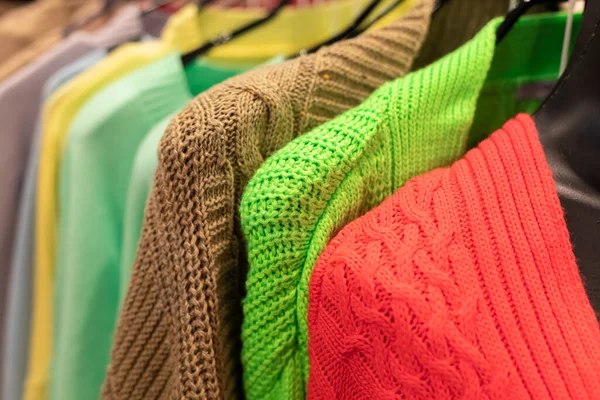 Parlak renklerden örülmüş süveterler bir mağazadaki askılarda kırmızı, yeşil ve kahverengi. — Stok fotoğraf