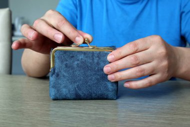 Kadın elleri masanın üzerinde duran mavi cüzdanı açar.
