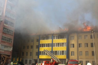 Çok katlı bir bina yanıyor ve yakınlarda yangını söndürmek için itfaiye araçları var.