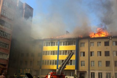 Çok katlı bir bina yanıyor ve yakınlarda yangını söndürmek için itfaiye araçları var.