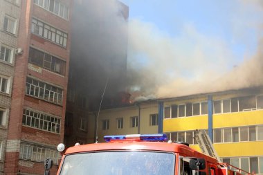 Çok katlı bir bina yanıyor ve yakınlarda yangını söndürmek için itfaiye araçları var.