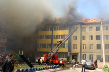 Çok katlı bir bina yanıyor ve yakınlarda yangını söndürmek için itfaiye araçları var.