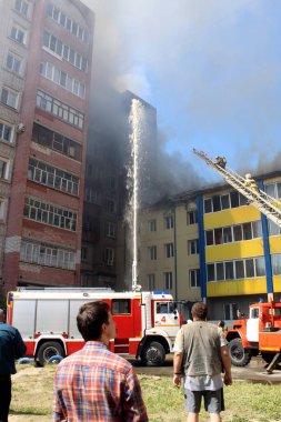 Çok katlı bir bina yanıyor ve yakınlarda yangını söndürmek için itfaiye araçları var.