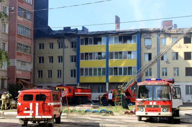 Çok katlı bir bina yanıyor ve yakınlarda yangını söndürmek için itfaiye araçları var.