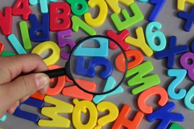 Sayılar ve harfler üzerinde bir büyüteç tutan kadın el.