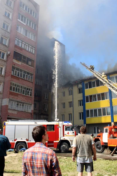Çok katlı bir bina yanıyor ve yakınlarda yangını söndürmek için itfaiye araçları var.